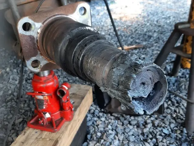 A red hydraulic jack sitting on a wooden block next to a piece of metal.